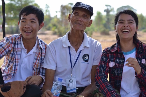 Photo of Mister YUM and two students on a swing laughing during the visit of the CEDAC Organic Farm in Takeo Province Cambodia.